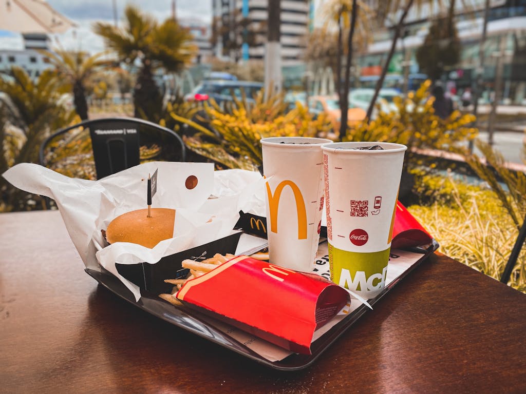 Appetitliches Fast-Food-Menü mit Burger, Pommes und Getränken auf einem Tisch im Freien in städtischer Umgebung