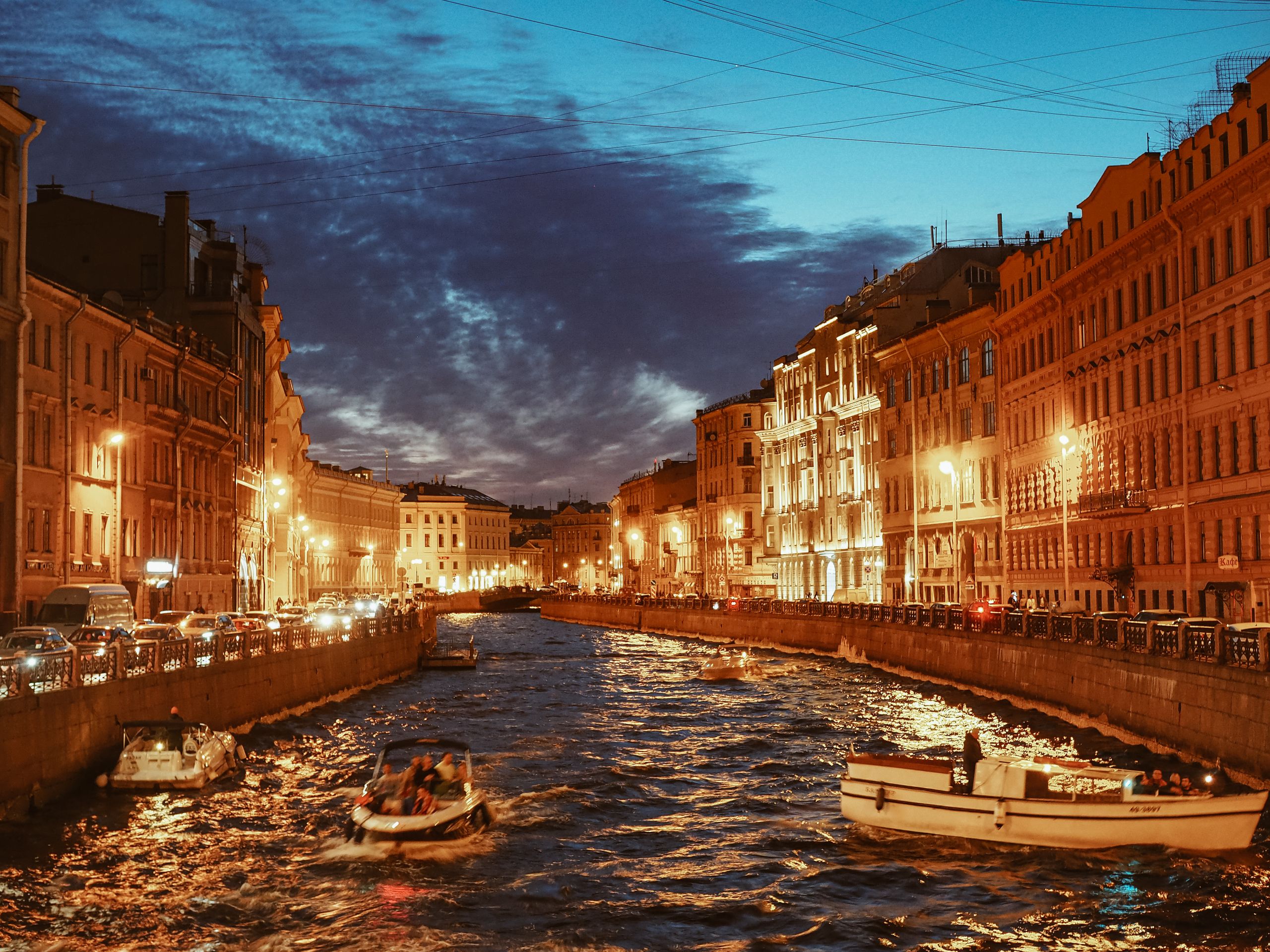 Blick in der Abenddämmerung auf einen Kanal in St. Petersburg mit beleuchteten Gebäuden und Booten