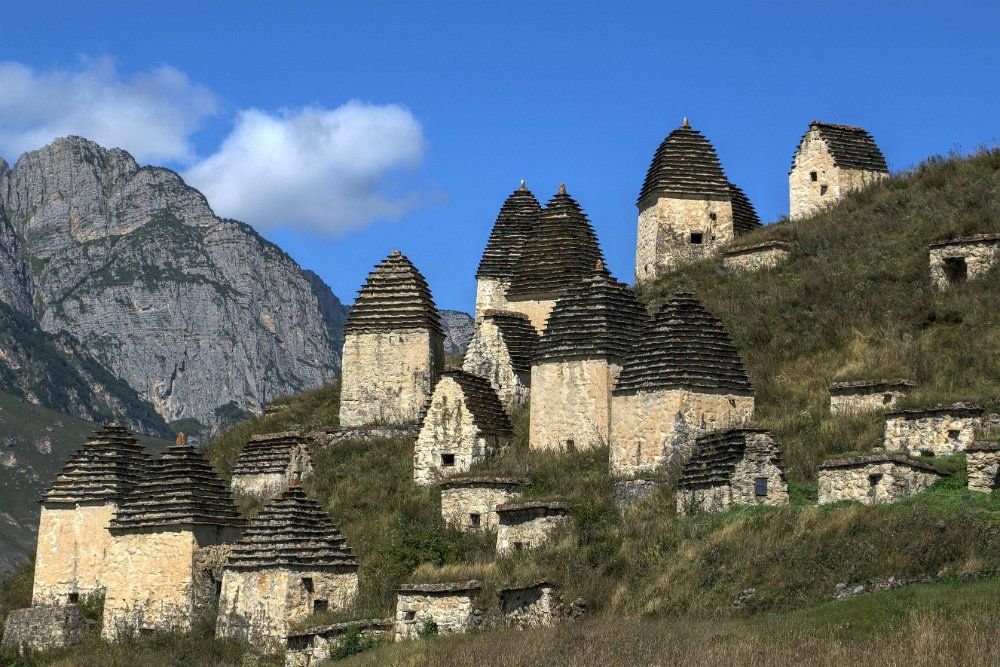 Alte Grabbauten aus Stein an einem grünen Berghang im Nordkaukasus, mit Felsgipfeln im Hintergrund